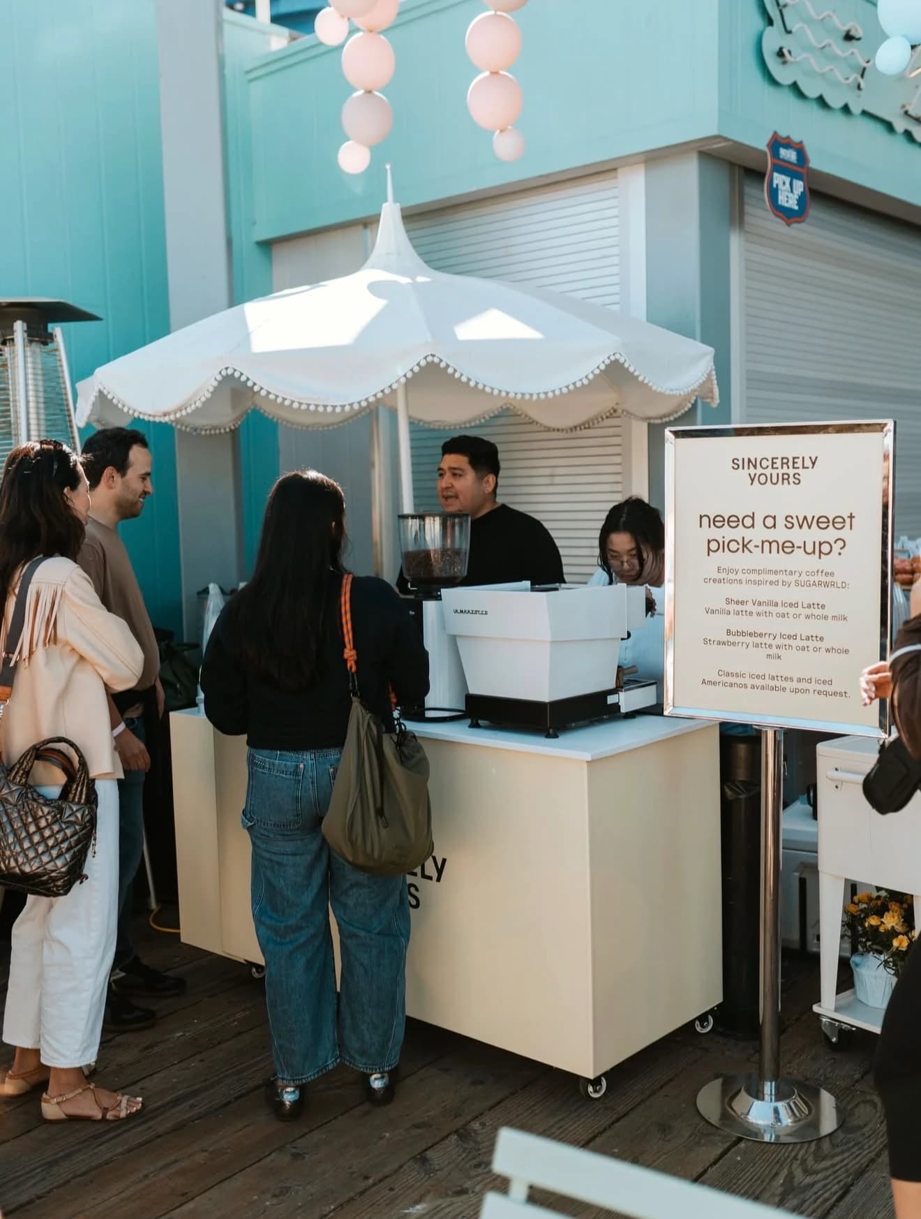 Pastel coffee cart with a scalloped white umbrella serving iced lattes on a boardwalk
