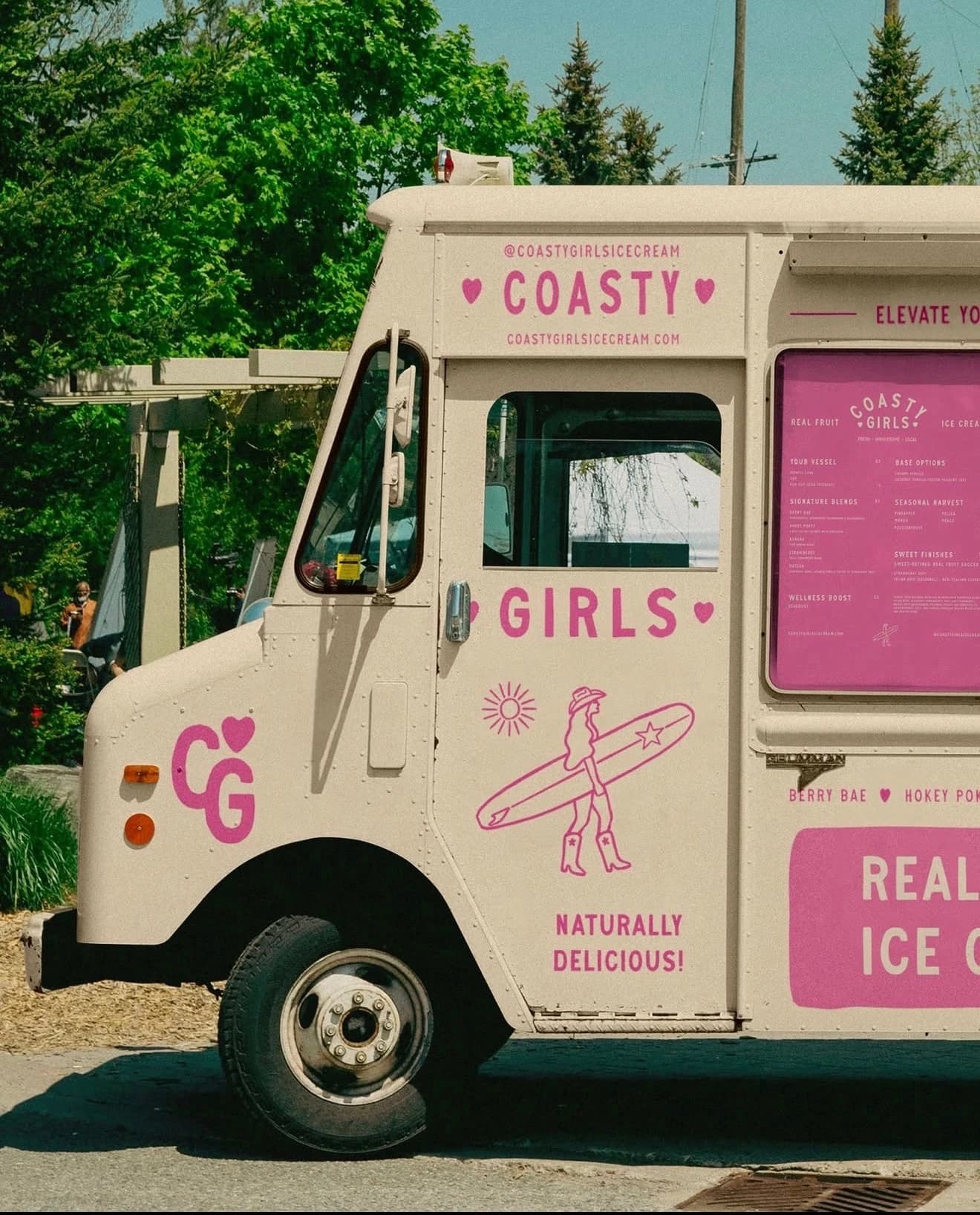 Vintage ice-cream truck with playful pink lettering parked by the trees