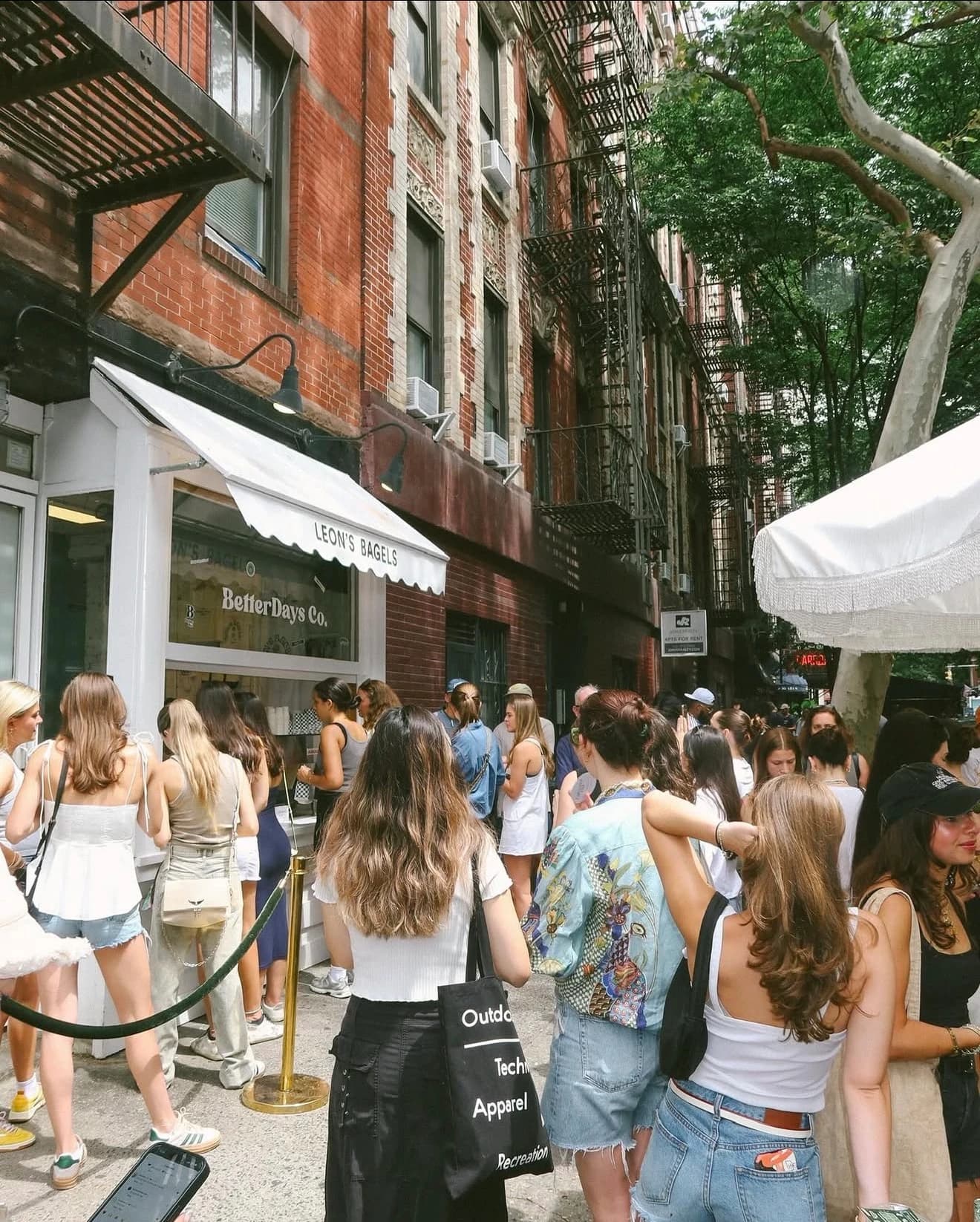 Group of friends waiting in line at a bagel shop pop-up on a sunny street