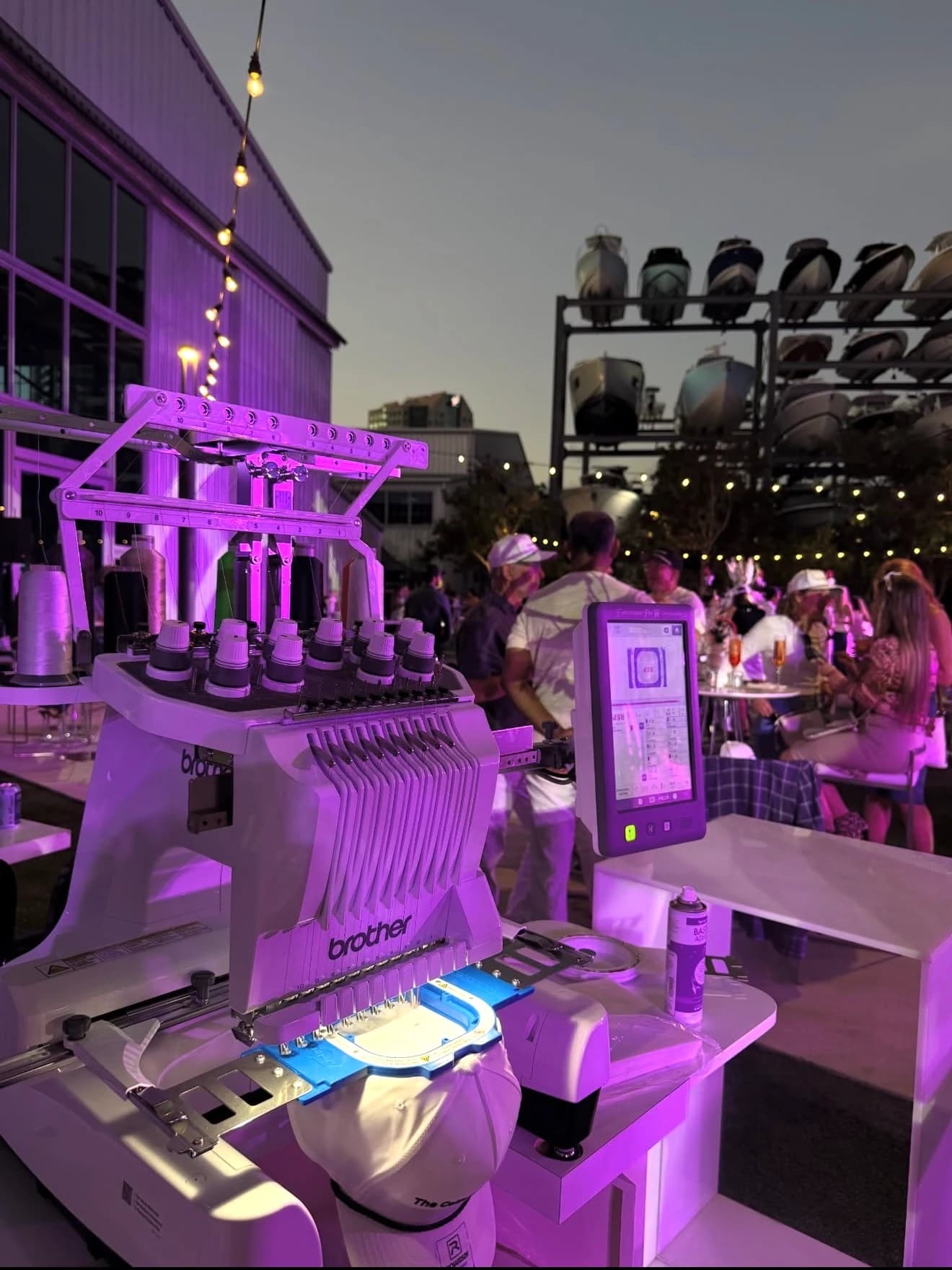 Evening waterfront pop-up event with custom cap embroidery under string lights